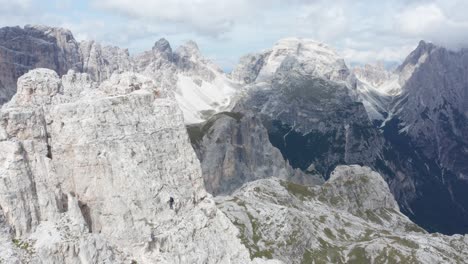 Mountain-climber-ascending-mountain-peak-in-Tre-Cime,-Dolomites,-aerial-dolly-out