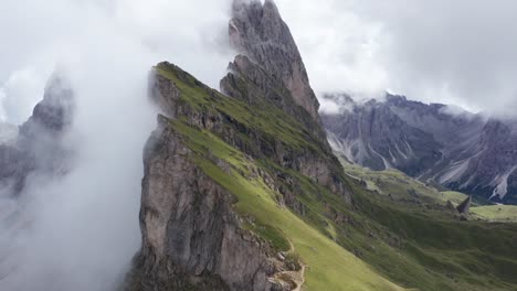 Drone-forward-flight-along-green-scenic-mountains-covered-by-dense-clouds-at-Puez-National-Park,Dolomites