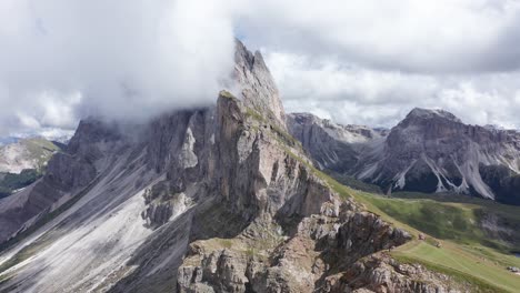 Person-standing-on-edge-of-mountain-peak-after-hiking-Seceda-Ridgeline-in-Italy---Spectacular-view-into-valley-during-summer-day-with-clouds-at-sky