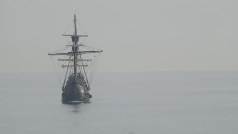 Ferdinand-Magellan-Nao-Victoria-carrack-boat-replica-with-spanish-flag-sails-in-the-mediterranean-at-sunrise-in-calm-sea-front-shot-turning-in-slow-motion-60fps