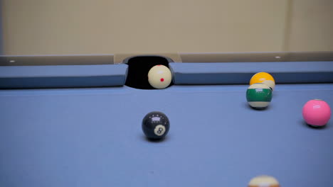 Cue-ball-hitting-many-pool-balls-near-table-hole-on-a-blue-baize-billiard-table
