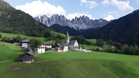 Idyllic-mountain-village-with-church-in-Dolomite-mountains,-aerial-orbit