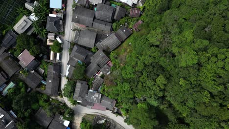 Forward-aerial-flight-looking-down-at-wooden-houses-next-to-dense-green-jungle