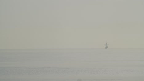 Ferdinand-Magellan-Nao-Victoria-carrack-boat-replica-sails-in-the-distance-in-the-mediterranean-at-sunrise-while-a-bird-flies-in-calm-sea-in-slow-motion-60fps