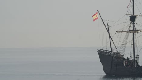 Ferdinand-Magellan-Nao-Victoria-carrack-boat-replica-sails-in-the-mediterranean-at-sunrise-in-calm-sea-side-shot-exiting-the-frame-in-slow-motion-60fps
