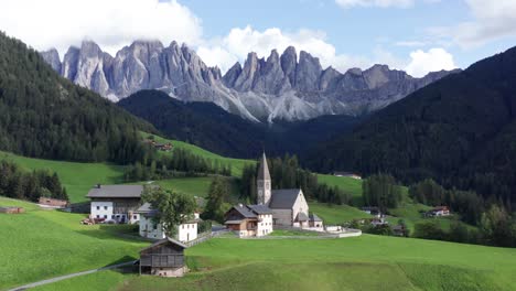 Small-mountain-village-with-church-under-Dolomites-mountains-in-Italy,-Val-Di-Funes-aerial