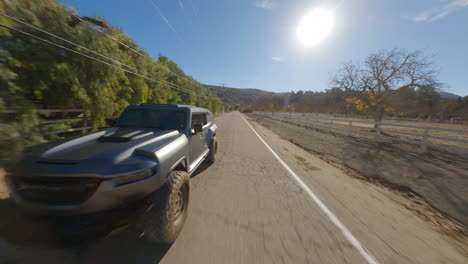 Reverse-FPV-view-of-an-off-roader-jeep-running-on-an-isolated-countryside-road-during-bright-sunny-day