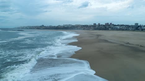 Drone-aerial-view-coast-seascape-beach,-atlantic-ocean-waves-wash-on-shore,-city-town-porto-portugal-background