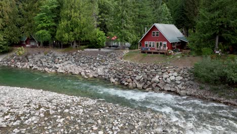 Aerial-view-of-a-quaint-red-cabin-overlooking-the-Skykomish-River-in-Baring,-Washington