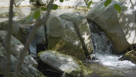 Panning-shot-of-small-cascade-pouring-into-river-on-a-sunny-day-located-in-Santa-Paula-Punch-Bowls-Southern-California