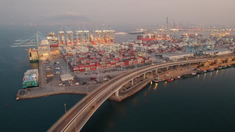 Highway-curving-around-stacked-shipping-containers-and-loading-cranes-at-Port-of-Algeciras,-Cadiz-aerial-orbiting-view