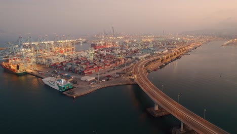 Aerial-view-of-Algeciras-port,-close-to-the-container-terminal-with-some-vessel-alongside-and-the-bridge-that-connects-the-port-to-the-city