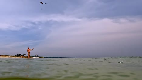 Half-underwater-view-of-adult-man-on-summer-vacation-in-swimsuit-on-beach-seashore-playing-with-toy-kite