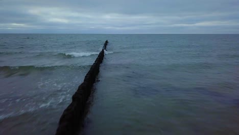 Establishing-aerial-view-of-Baltic-sea-coast-on-a-overcast-day,-old-wooden-pier,-white-sand-beach,-low-waves-crushing-against-the-coast,-climate-changes,-wide-angle-drone-shot-moving-forward
