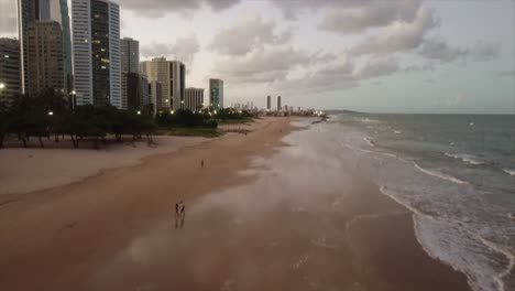Strandaufnahme-Nach-Wellen,-Die-Bis-Zu-Wolkenkratzern-Und-Flauschigen-Wolken-In-Brasilien-Schwenken