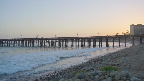 Panning-shot-of-waves-of-the-Pacific-Ocean-crashing-along-the-shores-of-Ventura-Pier-as-the-sun-sets-located-in-Southern-California