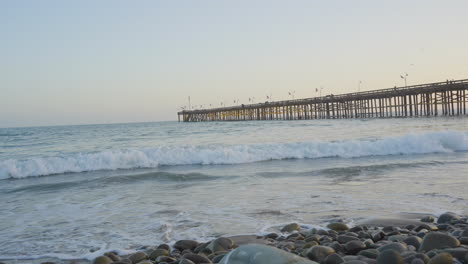 Panning-shot-of-waves-at-sunset-rolling-though-the-Pacific-Ocean-with-the-Ventura-Pier-in-the-background-located-in-Southern-California