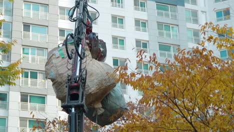 Bags-Of-Garbage-Being-Lifted-And-Transported-Over-Yellow-Autumn-Tree-By-Man-operated-Garbage-Truck-With-Claw-Arm