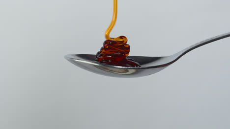 Sweet-golden-honey-dripping,-healthy-liquid-nectar-flowing-onto-a-metal-spoon-and-dropping-down