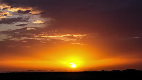Zeitraffer-Ansicht-Von-Goldenen-Orangefarbenen-Sonnenstrahlen,-Die-Durch-Die-Wolkenlandschaft-über-Die-Silhouettierte-Landschaft-Fließen