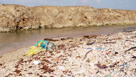 Breite-Wanne-Aus-Künstlichen-Plastikabfällen-Und-Müll,-Die-Langsam-An-Der-Felsigen-Küste-In-Der-Karibik-Angespült-Werden