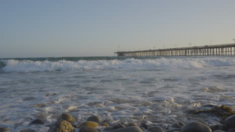 Panning-shot-of-the-end-of-Ventura-Pier-panning-into-the-Pacific-Ocean-with-huge-waves-crashing-into-the-shores-of-Ventura-Beach-at-sunset-located-in-Southern-California