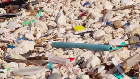 Close-up-slow-pan-of-man-made-plastic-debris-and-rubbish-slowly-being-washed-up-on-rocky-shore-in-the-Caribbean