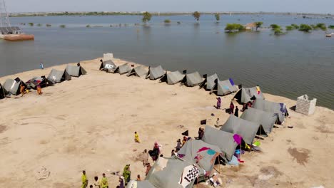 Vista-Aérea-Del-Campamento-Improvisado-Con-Tiendas-De-Campaña-Para-Albergar-A-Los-Refugiados-De-Las-Inundaciones-Al-Lado-De-Una-Carretera-Elevada-Rodeada-De-Aguas-Expansivas-En-La-Zona-Rural-De-Jacobabad,-Sindh
