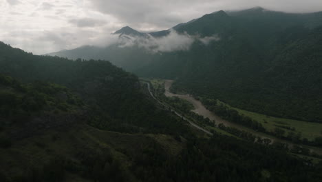 Flyover-above-a-road-alongside-the-Kura-river,-hidden-in-dark-Georgian-valley