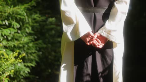 Close-up-shot-of-the-hands-of-a-monk-walking-in-the-forest-towards-the-light