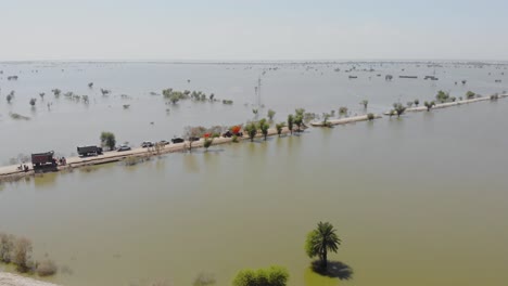 Aerial-Flying-Towards-Road-With-Line-Of-Cars-And-Trucks-Surrounded-By-Flooded-Landscape-In-Jacobabad,-Sindh