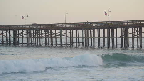 Panning-shot-of-huge-waves-rolling-though-the-Pacific-Ocean-along-Ventura-Pier-as-the-sun-sets-in-the-background-located-in-Southern-California