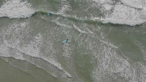 Slow-motion-aerial-top-down-shot-of-surfers-going-through-the-ocean-waves-in-Costa-Mesa,-California