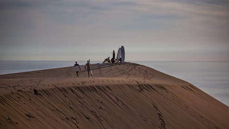 Silhouette-Einer-Gruppe-Junger-Erwachsener-Sanddünensurfen-In-Marokko-Mit-Dem-Ozean-Im-Hintergrund---Zeitraffer