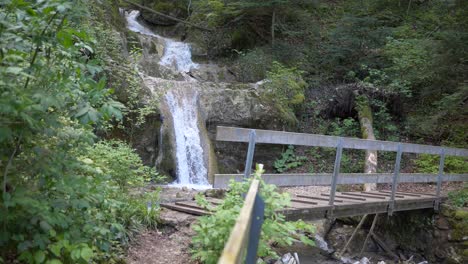 Super-slow-motion-shot-of-flowing-waterfall-down-the-mountain-and-wooden-bridge