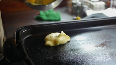 Pancake-waffle-mix-being-placed-onto-hot-pan-using-nylon-flex-turning-spoon-filmed-as-close-up