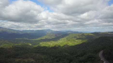 Impresionantes-Vistas-Desde-Un-Vuelo-De-Drones-De-Un-Valle-De-Color-Verde-Vivo,-Con-Nubes-En-El-Cielo-Y-Una-Imponente-Cordillera-En-El-Fondo