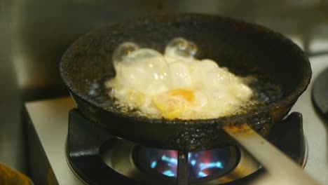 Egg-being-oil-fried-and-flipped-in-frying-pan-on-gas-fire-stove-filmed-in-close-up