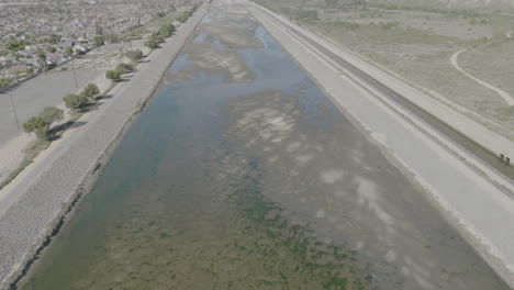 Aerial-shot-of-a-river-with-a-pan-up-revealing-a-bridge-in-Costa-Mesa,-California