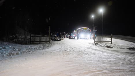Eine-Super-Breite-Gruppe-Von-Menschen,-Die-Mitten-In-Der-Nacht-Auf-Einem-Schneebedeckten-Parkplatz-Einen-Bus-Auspacken,-Während-Es-In-Norwegen-Schneit