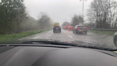 Driving-in-a-heavy-rain-storm-in-a-traffic-jam-on-the-road-in-England-with-the-windscreen-wipers-clearing-the-rainfall