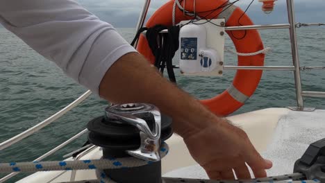 Tightening-a-rope-around-a-winch-on-a-sailboat-close-to-a-lifebuoy