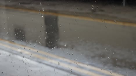 Regen-Fällt-Auf-Eine-Nasse-Straße,-Gesehen-Durch-Ein-Mit-Regentropfen-Bedecktes-Fenster