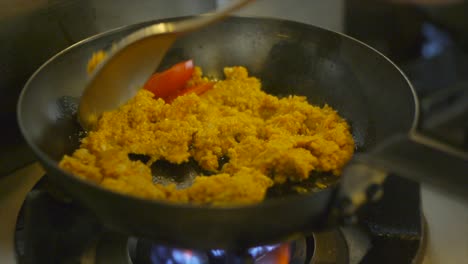 Couscous-being-stir-fried-in-frying-pan-with-spoon-on-gas-fire-stove-filmed-in-close-up