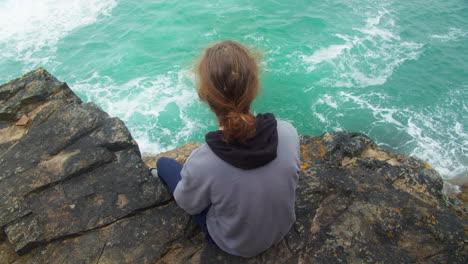 Depressed-Young-Person-Sitting-on-Coastal-Cliff-Edge-Watching-the-Ocean-Seeking-Peace-and-Calmness