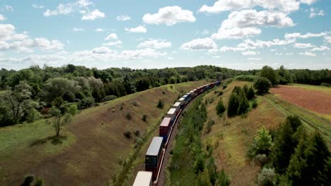 Endless-Freight-train-travels-through-grassy-valley-landscape-underneath-bridge-as-car-passes-on-road
