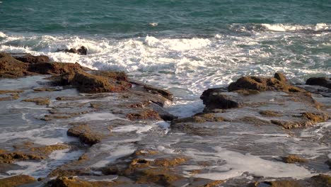 Waves-breaking-on-rocky-beach-cliffs-at-low-tide-in-slow-motion