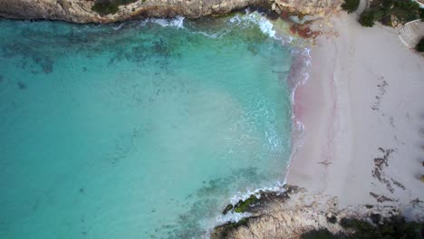 Drone-rises-above-turquoise-water-and-white-sand-beach-of-Cala-Anguila-Cove,-Mallorca