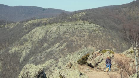 Woman-hiker-sits-on-stones-admiring-view-on-hike-trail,-jib-shot-hand-held