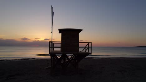 Lifeguard-House-silhouette,-colourful-dawn,-drone-orbit,-Cala-Millor-Mallorca